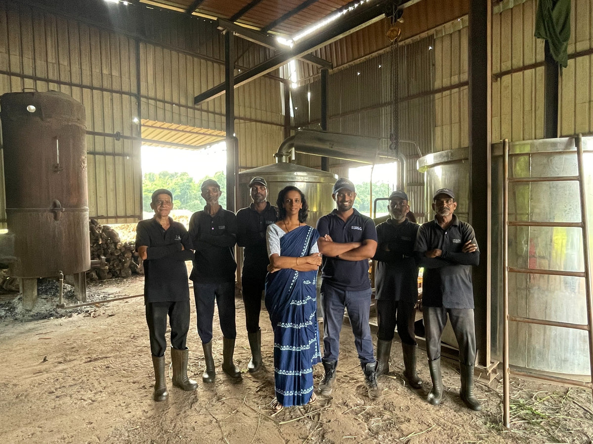 The Sugandha team standing together inside the distillation workshop, with the boiler and stainless steel vessels behind them.